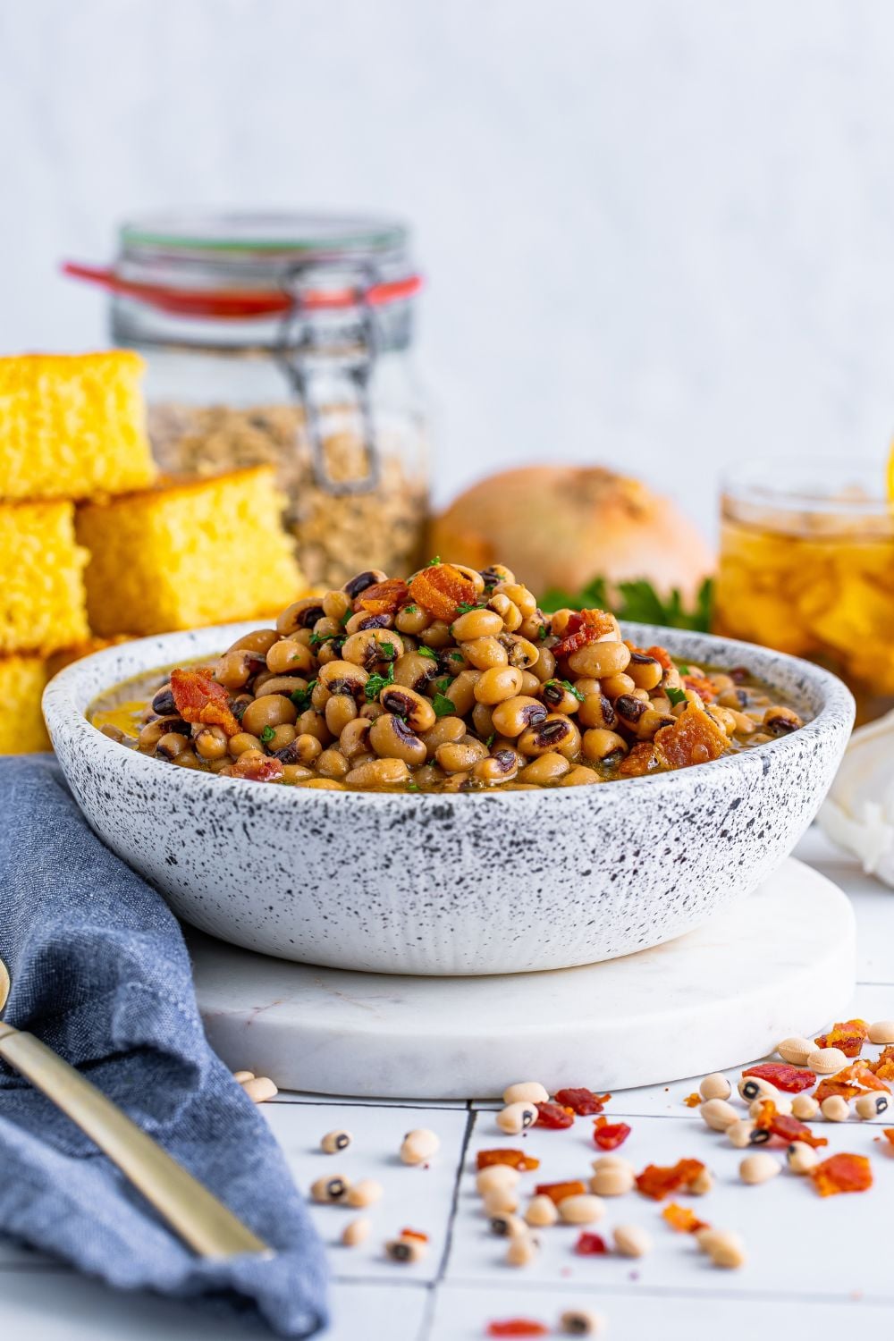 Black Eyed Peas in a small bowl with cornbread, onion, tea and more sitting around the bowl on the table