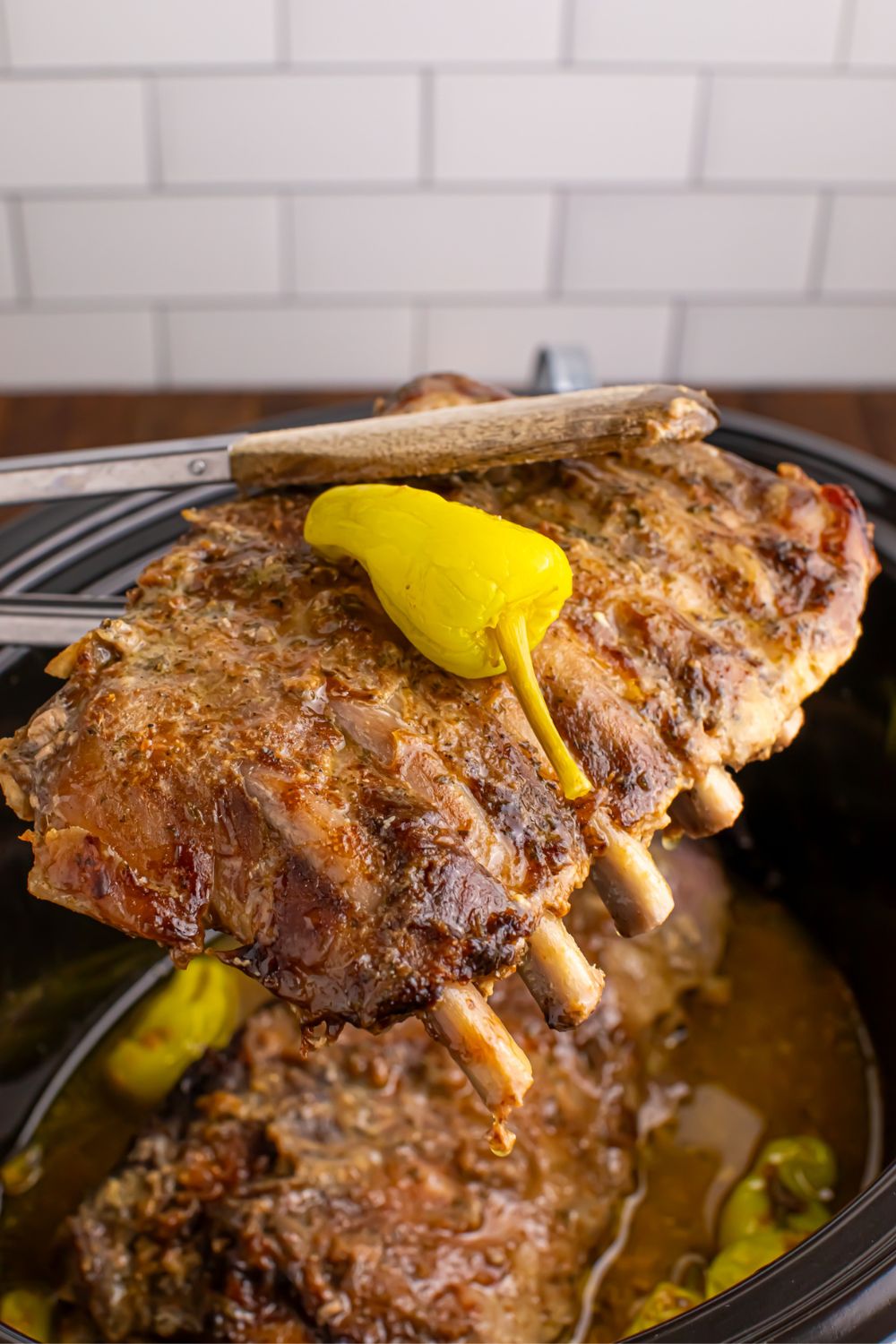 baby back ribs being held with tong above the slow cooker sitting on the table