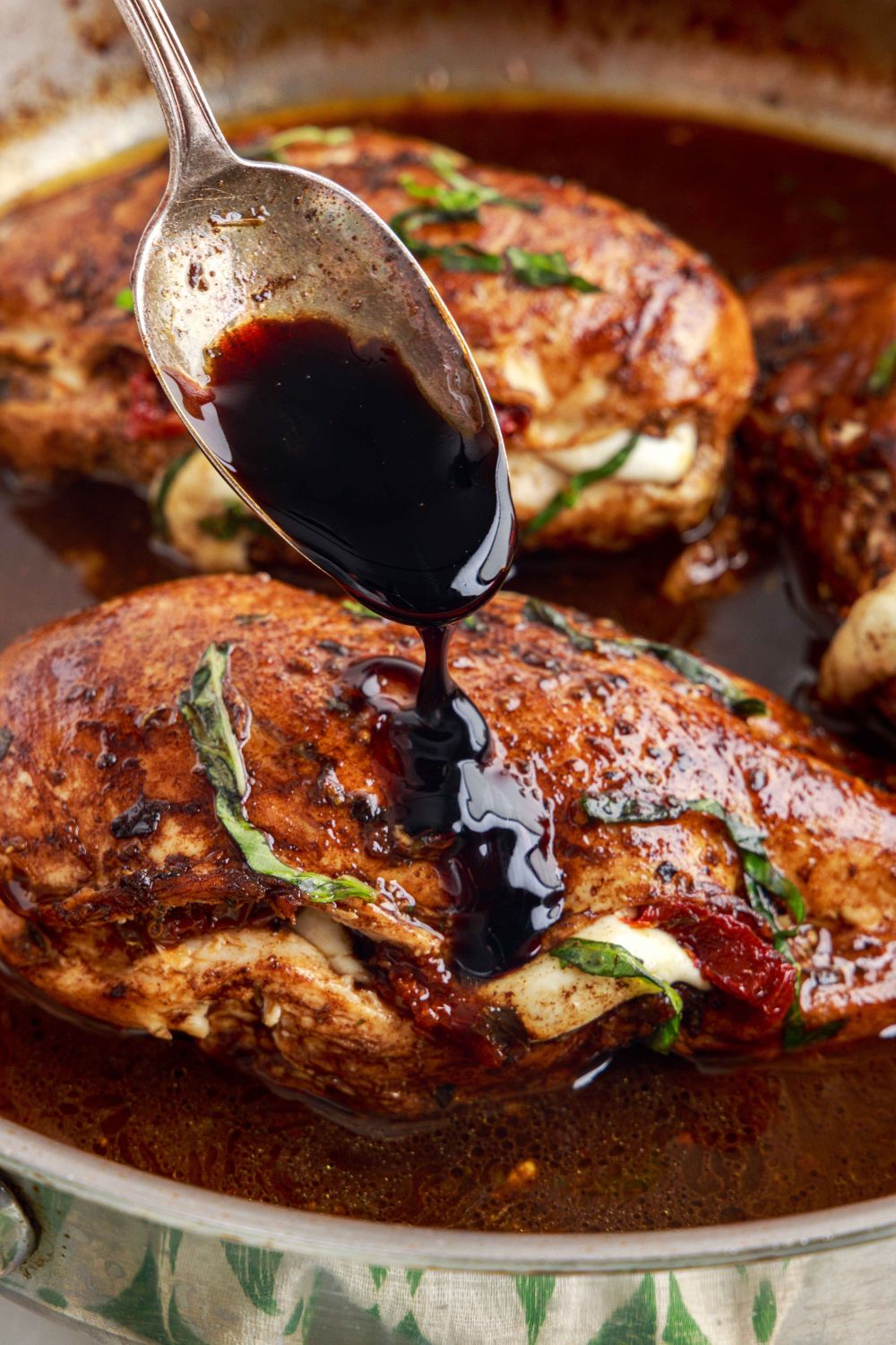Caprese Stuffed Chicken in a pan with a spoon drizzling on a balsamic glaze on top of chicken 