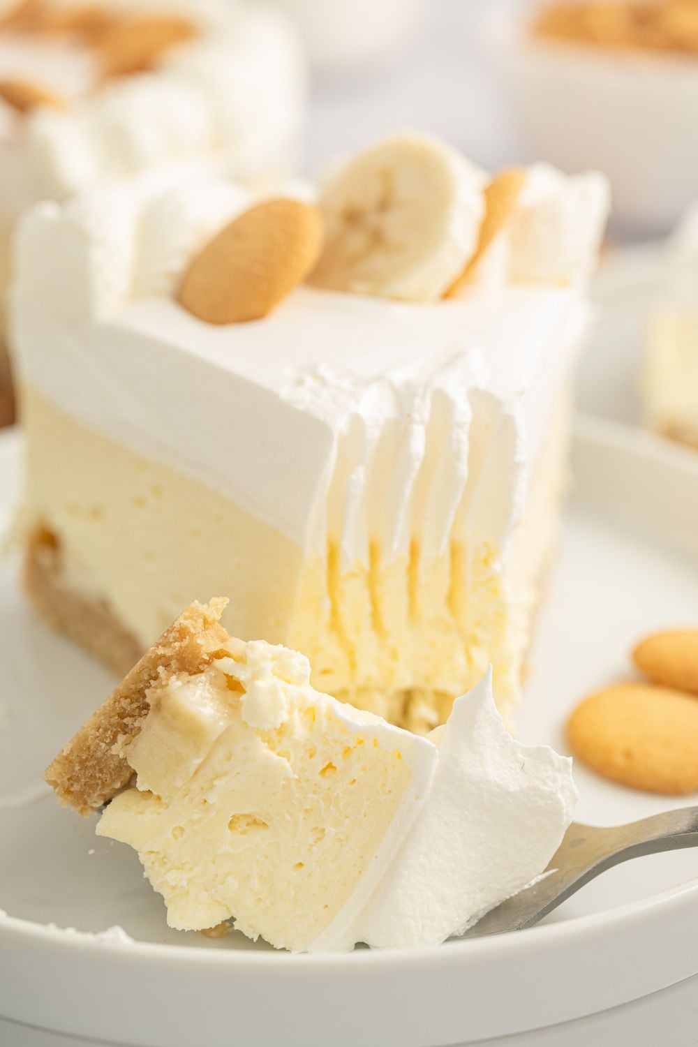slice of banana pudding cheesecake no bake on plate with a fork with a bite of cheesecake on it