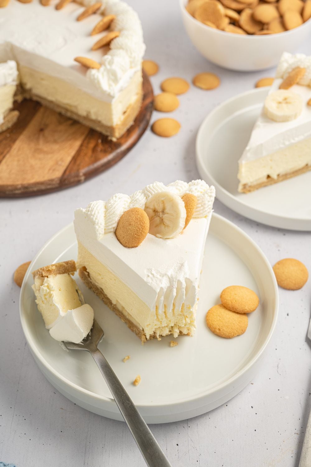 slices of No Bake Banana Pudding Cheesecake on plates and the whole cheesecake sitting in background