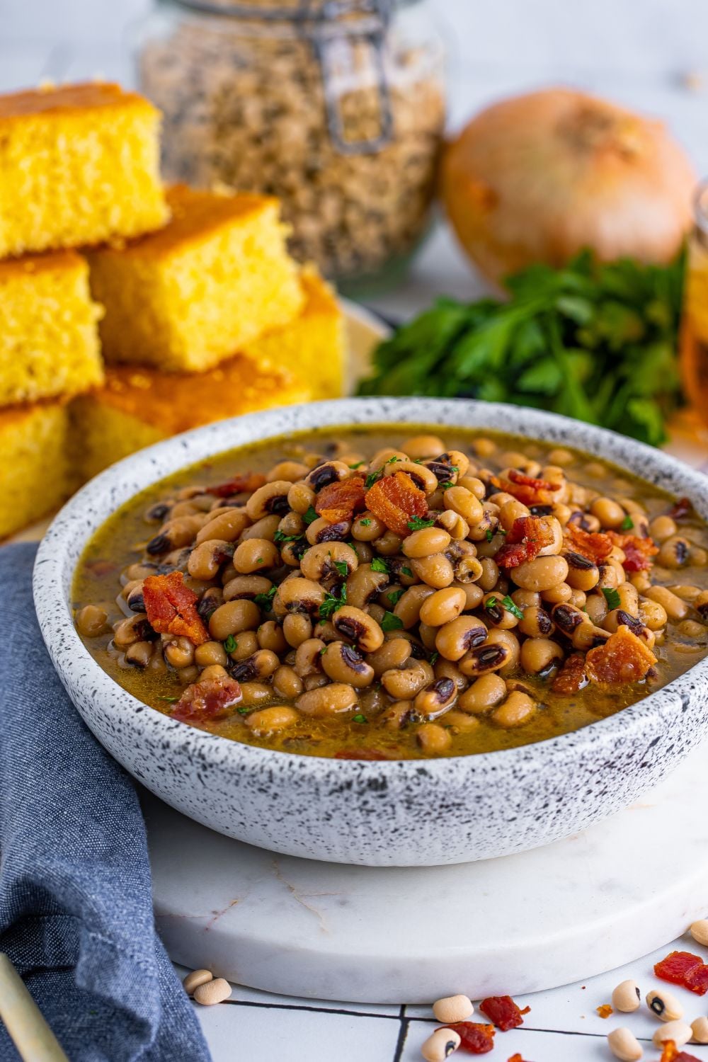 Black Eyed Peas in a bowl with a side view to see peas and ingreidents in bowl. the cornbread and parsley are sitting around the bowl 