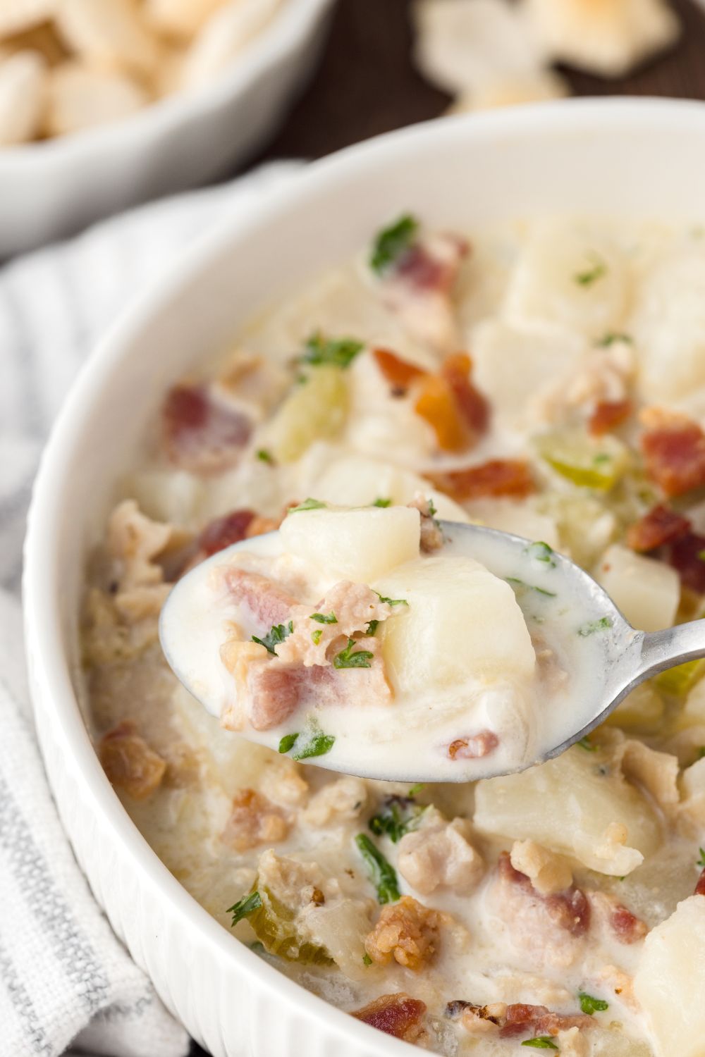bowl of New England Clam Chowder on table with a spoonful sitting above bowl to show the soup closer 