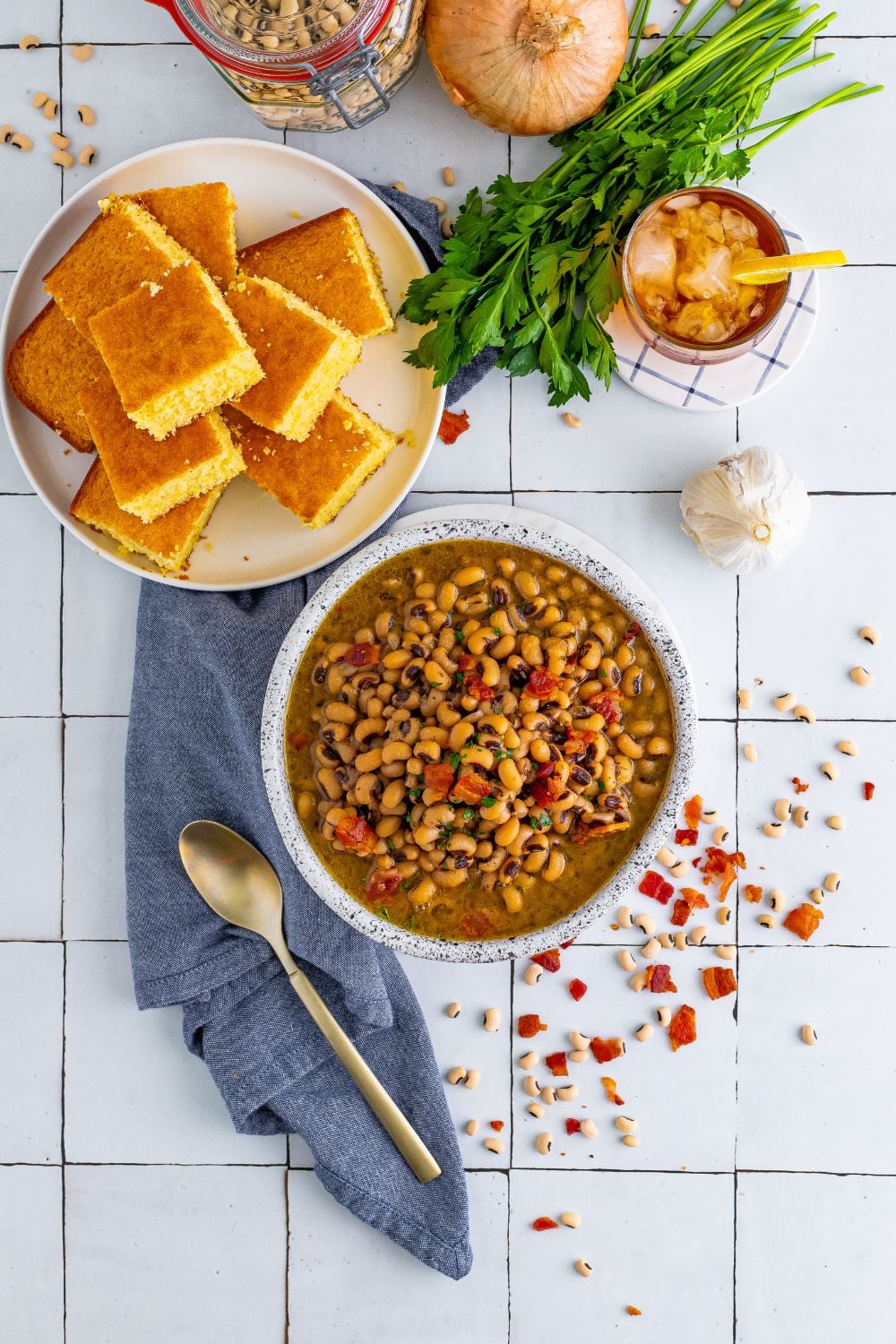 overhead look of black eyed peas in a bowl, plate of cornbread, and garnishes around plates