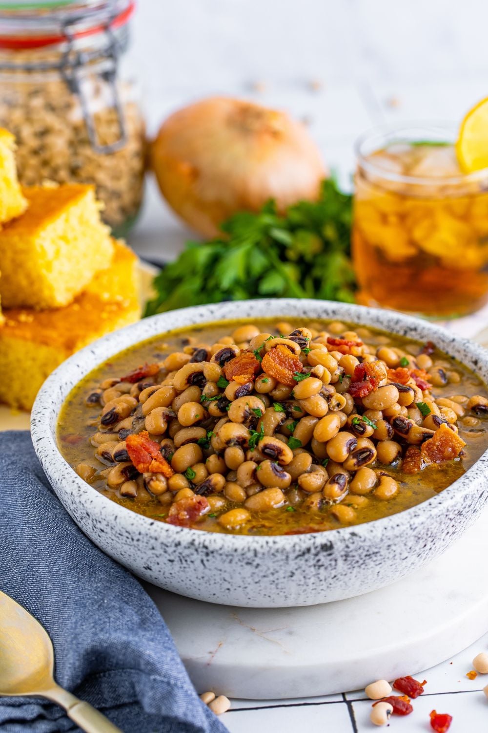 Black Eyed Peas in a bowl with cornbread, onion, parsley and a glass of tea sitting behind the bowl 