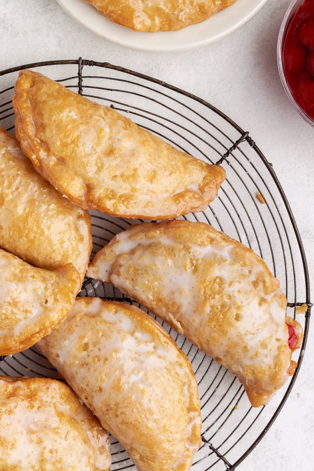 Cherry Cheesecake Hand Pies on a metal cooling rack sitting on table with bowls of ingredients around the cooling rack