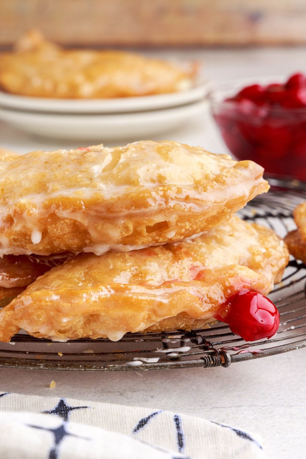 Cherry Cheesecake Hand Pies stacked on top of each other with some cherry pie filling in a glass bowl and sitting by the pies on table