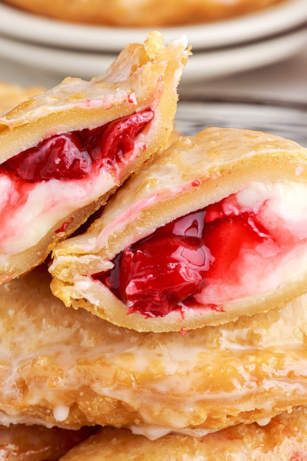 Cherry Cheesecake Hand Pies stacked on table and the top one cut in half to show the filling inside