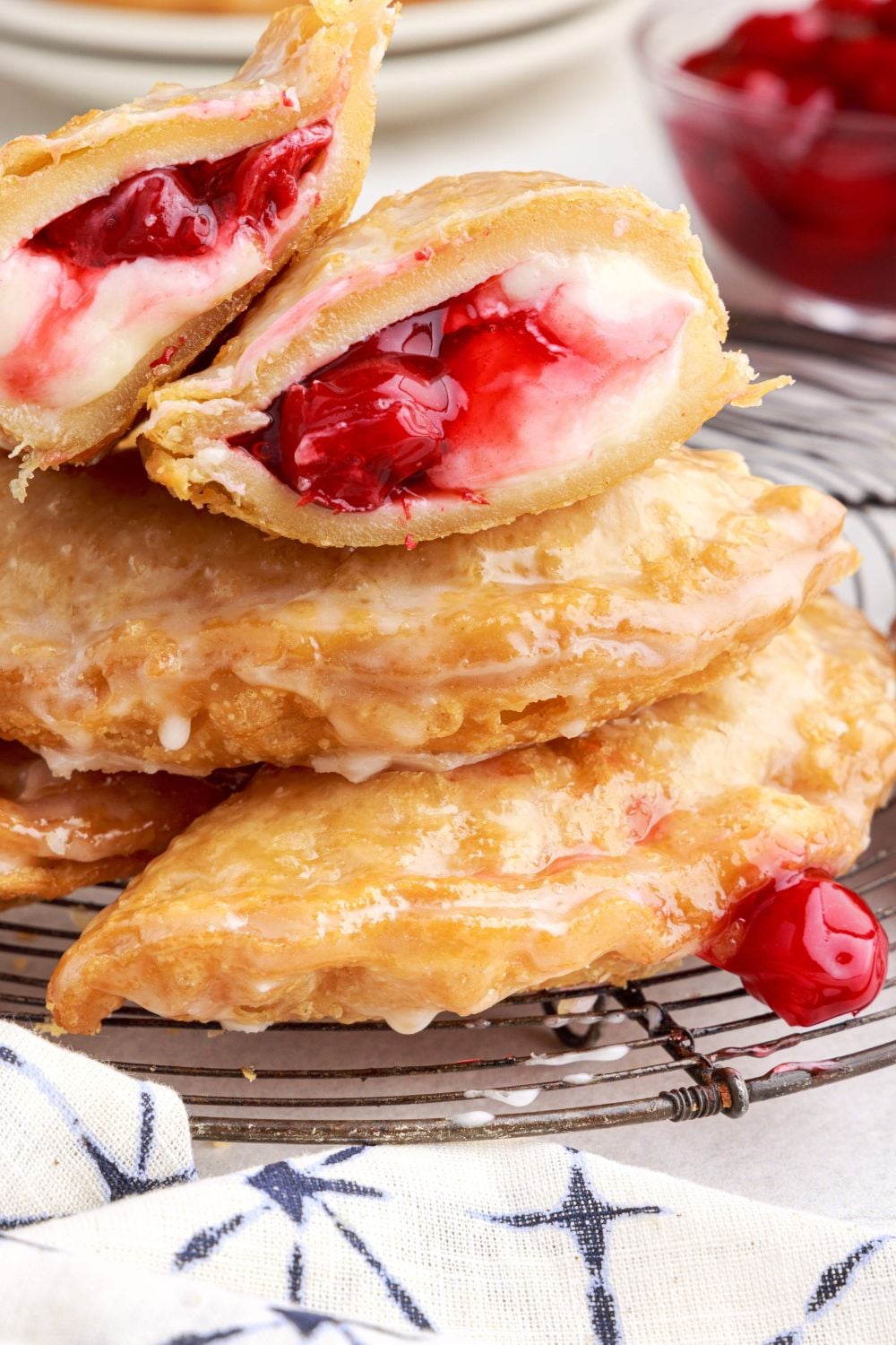 Cherry Cheesecake Hand Pies on a cooling rack stancked on top of each other, with one cut in half to show the sweet filling inside of cream cheese and cherries
