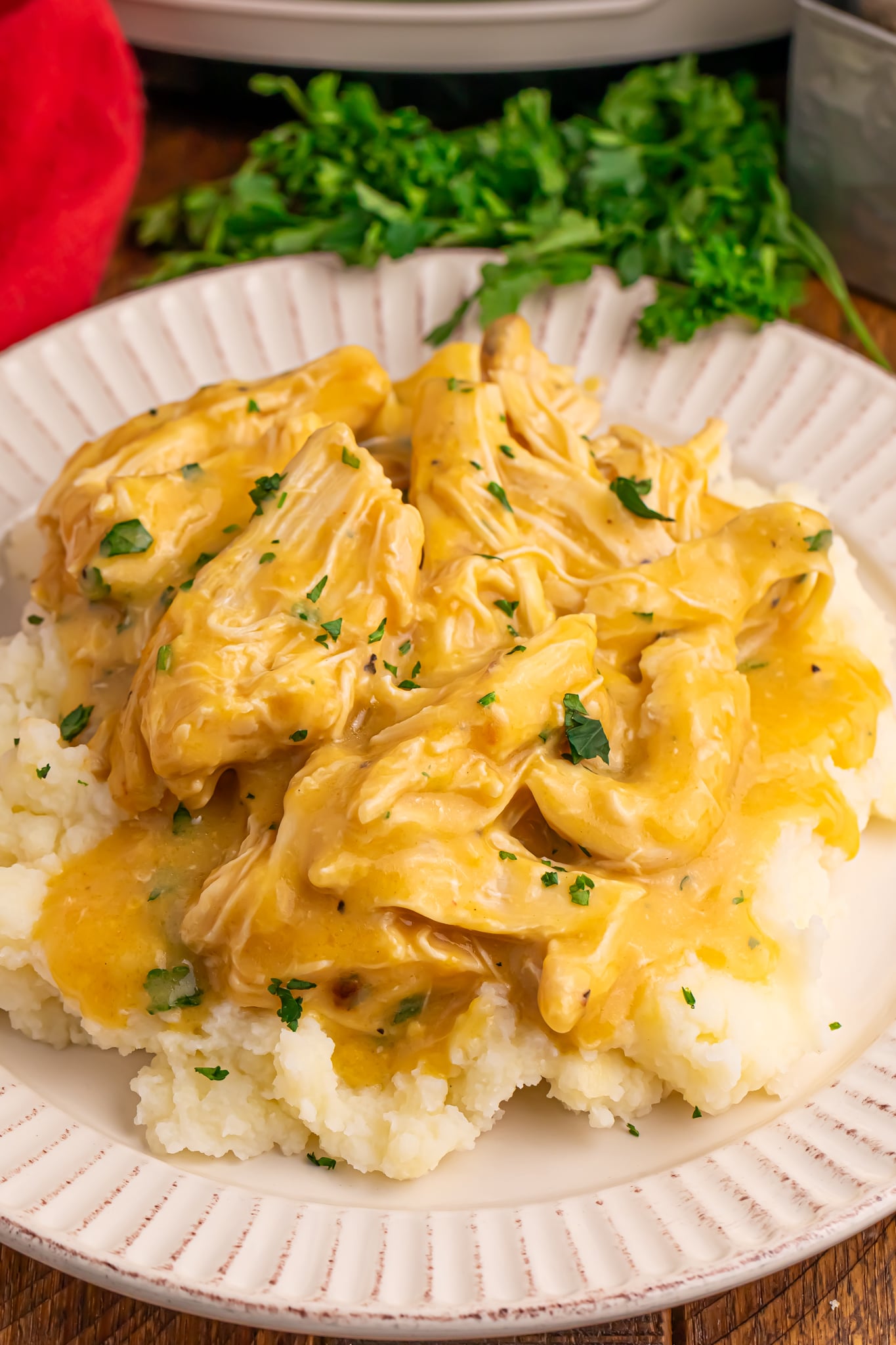 Crock Pot Chicken and Gravy on top of a bed of potatoes on a plate with parsley in the background