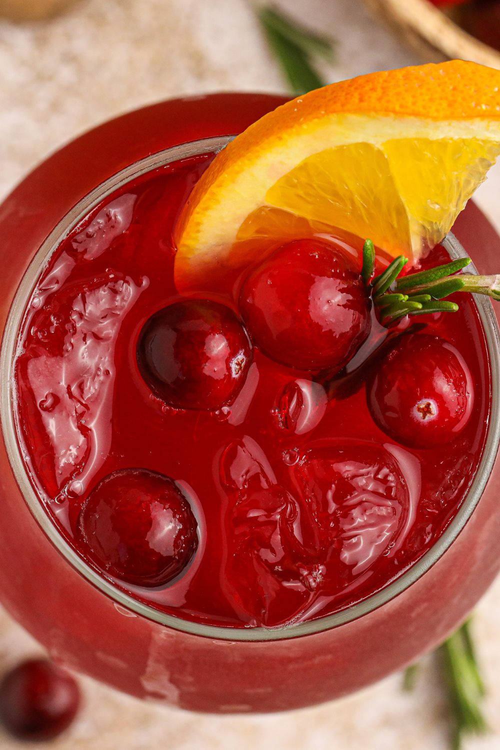 overhead look of cranberry cocktail in a glass with fresh cranberries and an orange slice in glass