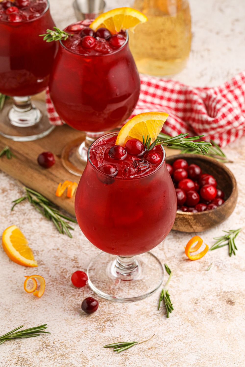 cocktail glasses filled with a cranberry whiskey sour and sliced oranges and cranberries scatterd on table