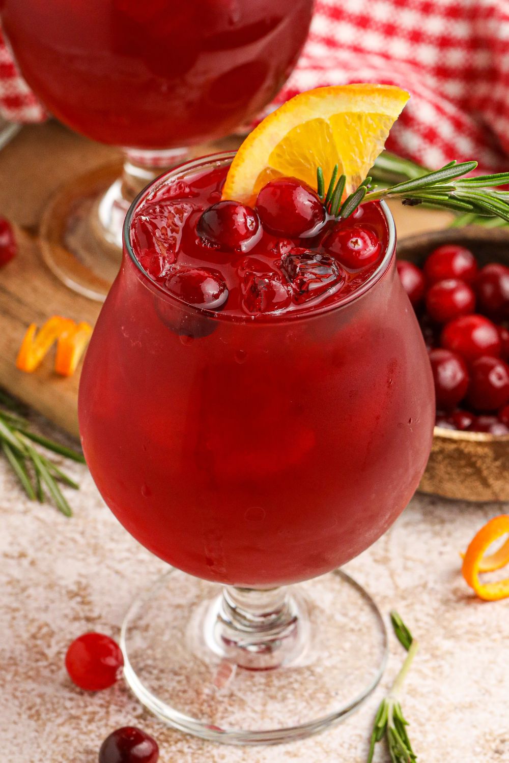 Cranberry Whiskey Sour in a cocktail glass garnished with cranberries, and an orange wedge on the glass