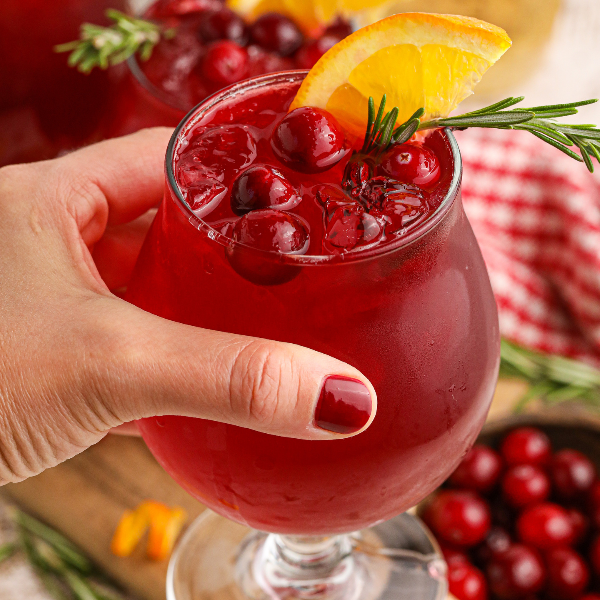 Cranberry Whiskey Sour cocktail in a glass being held in a ladies hand 