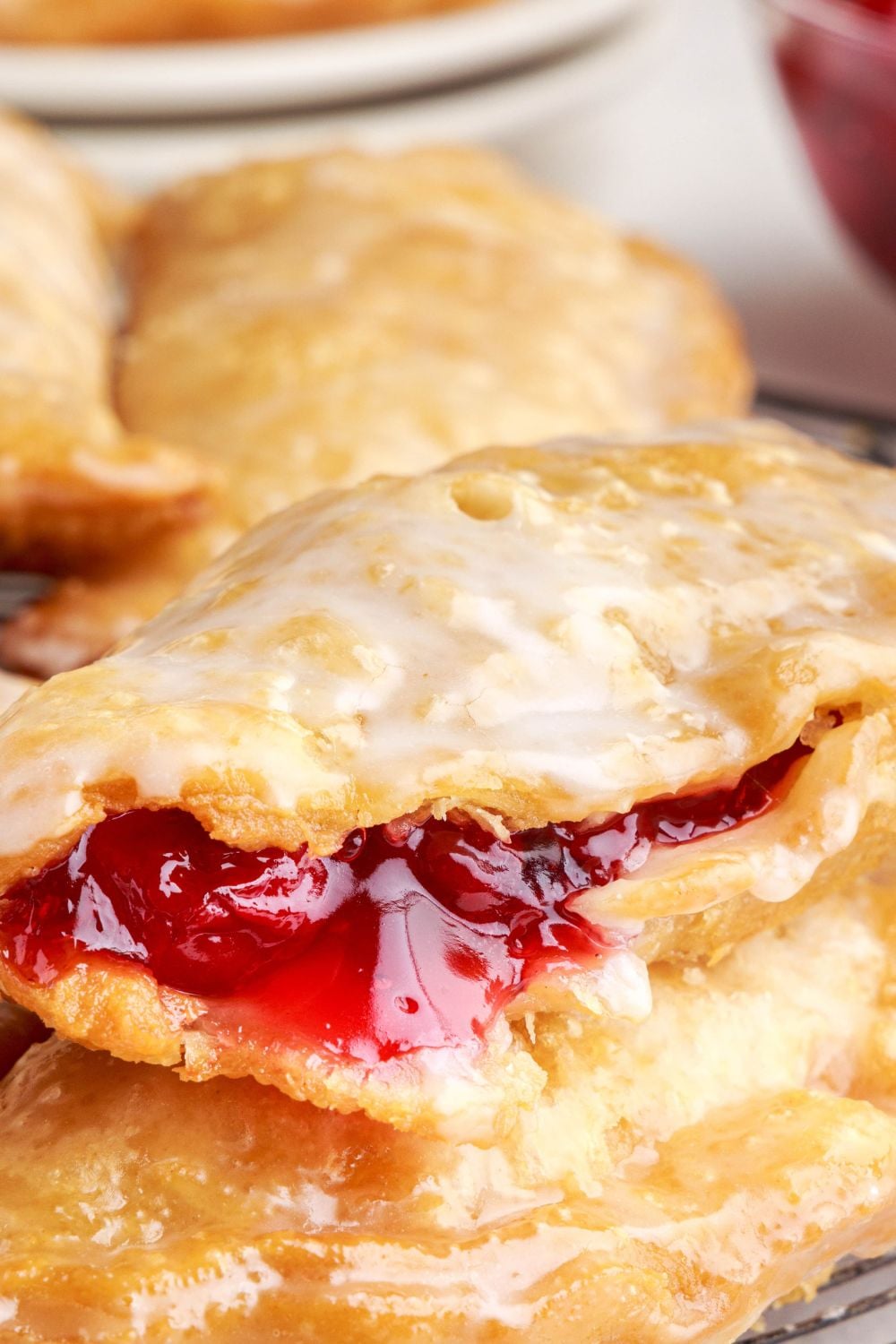 Cherry Cheesecake Hand Pies stacked on top of each other, with one split open showing a bit of the pie filling seeping out of the side of the pie