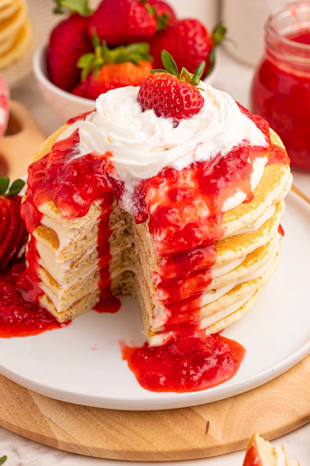 Strawberry Cheesecake Pancakes on plate with some cut out and whipped cream melting off the top