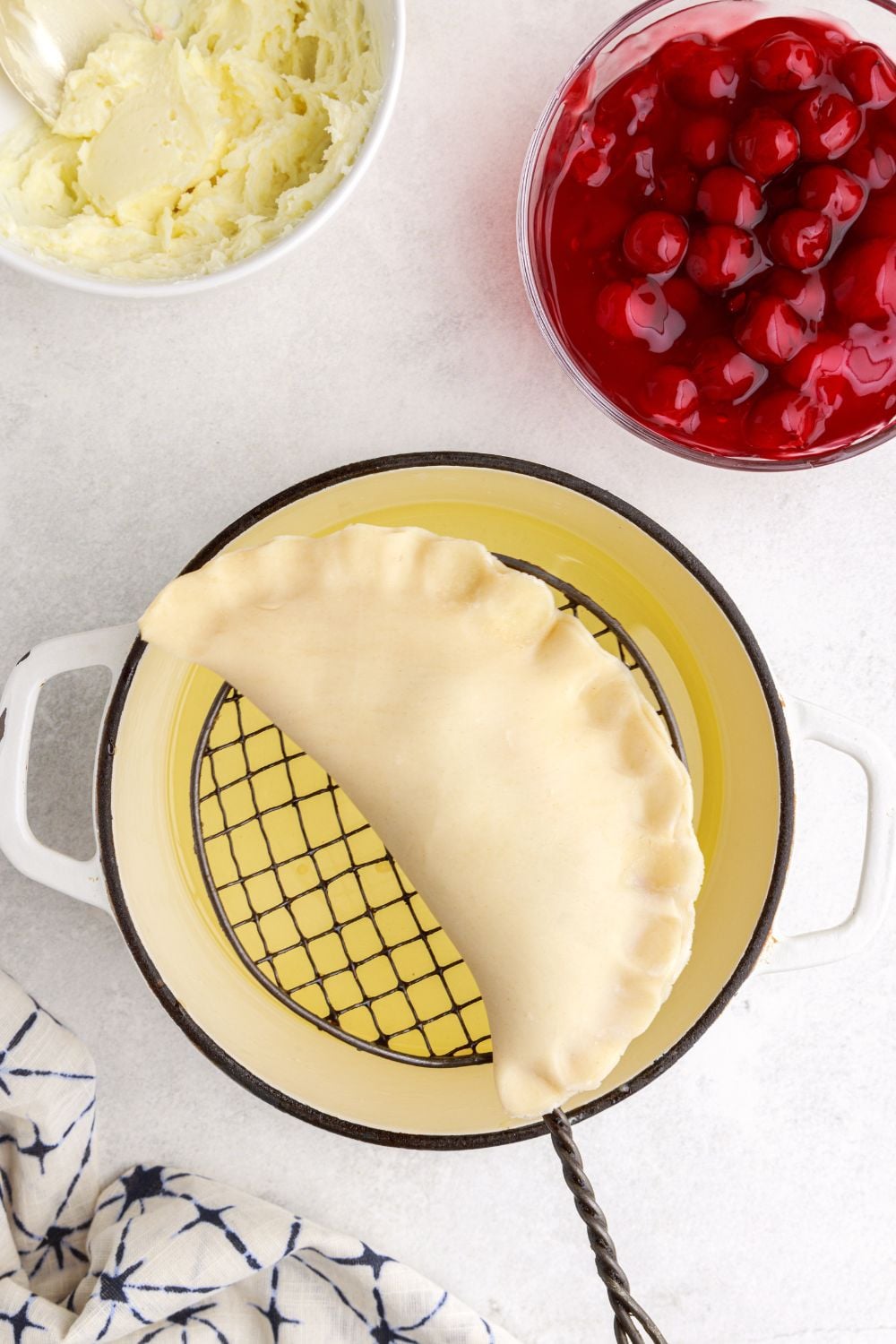 slotting spoon holding a raw Cherry Cheesecake Hand Pies over a pan of oil