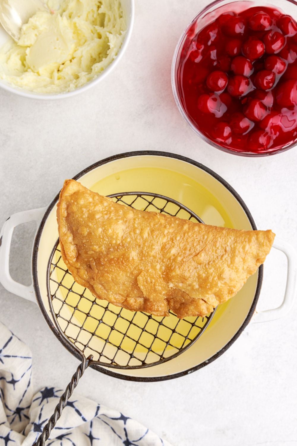 slotting spoon holding a fried Cherry Cheesecake Hand Pies over a pan of oil