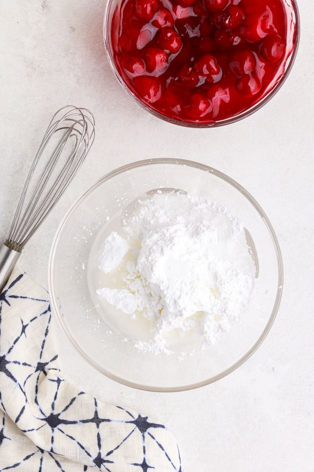 powdered sugar glaze ingredients in a glass bowl with a whisk by it and bowl of pie filling