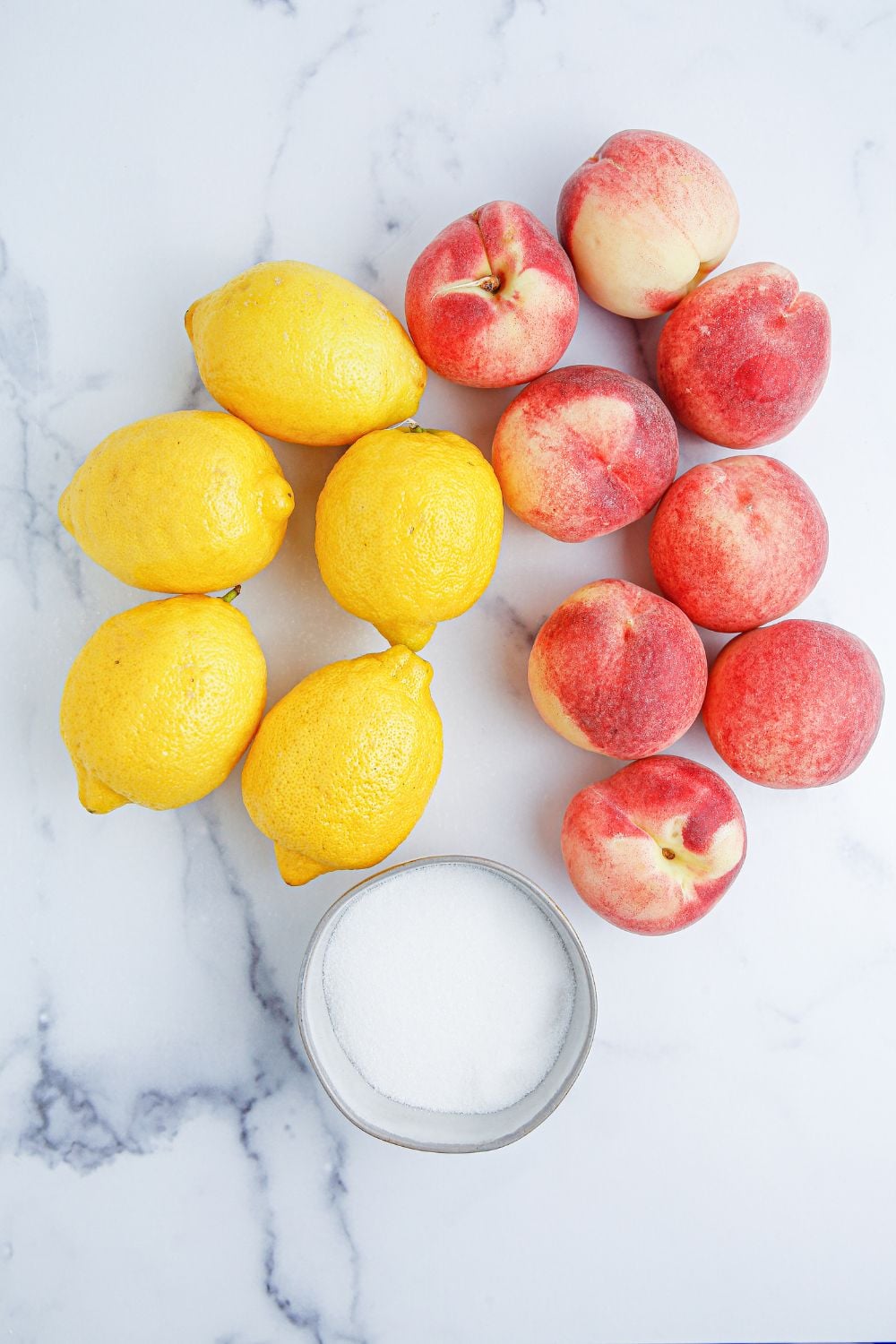 lemons, peaches, and a bowl of sugar sitting on a marble countertop