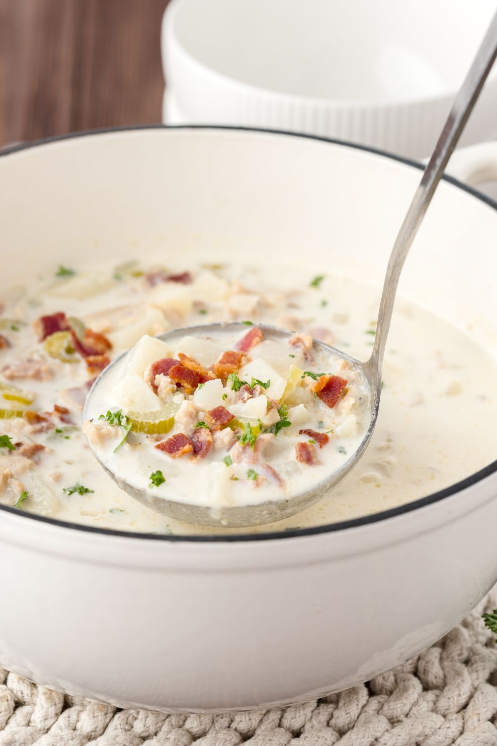 ladle full of clam chowder and a pot under full of chowder as well sitting on table