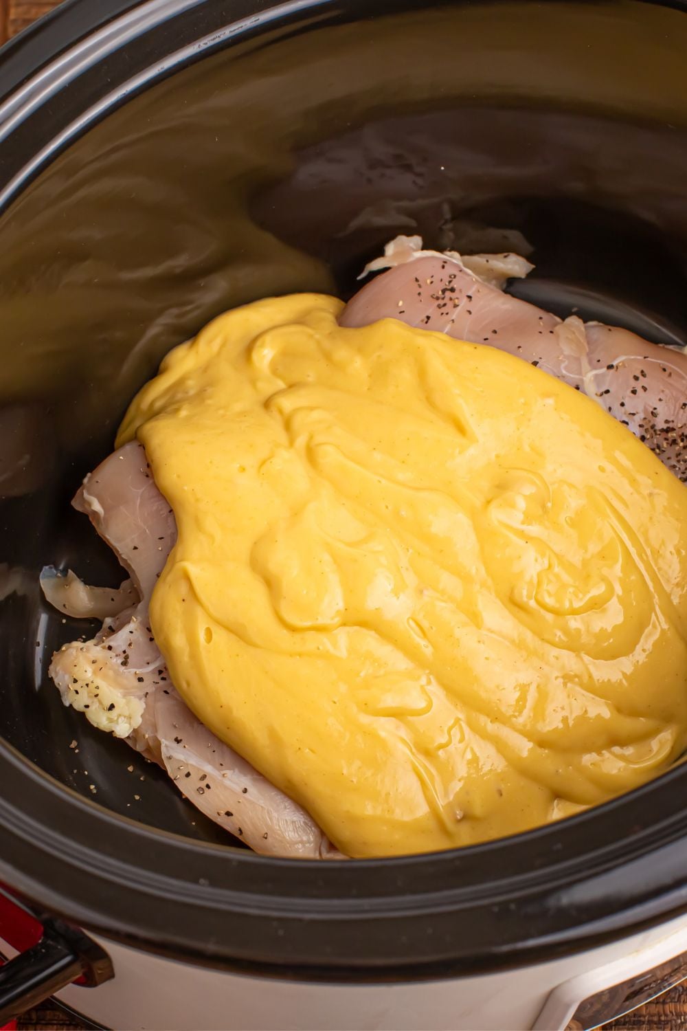 raw chicken in crockpot with a gravy and soup mixture poured over the top of the chicken