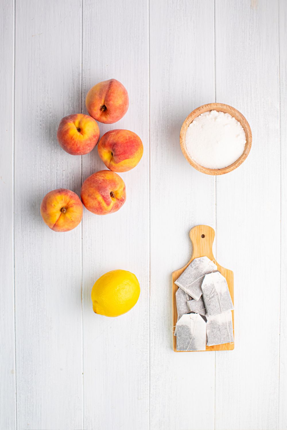 peaches, lemon, a bowl of sugar, and tea bags are sitting on a table to show ingredients for this peach sweet tea