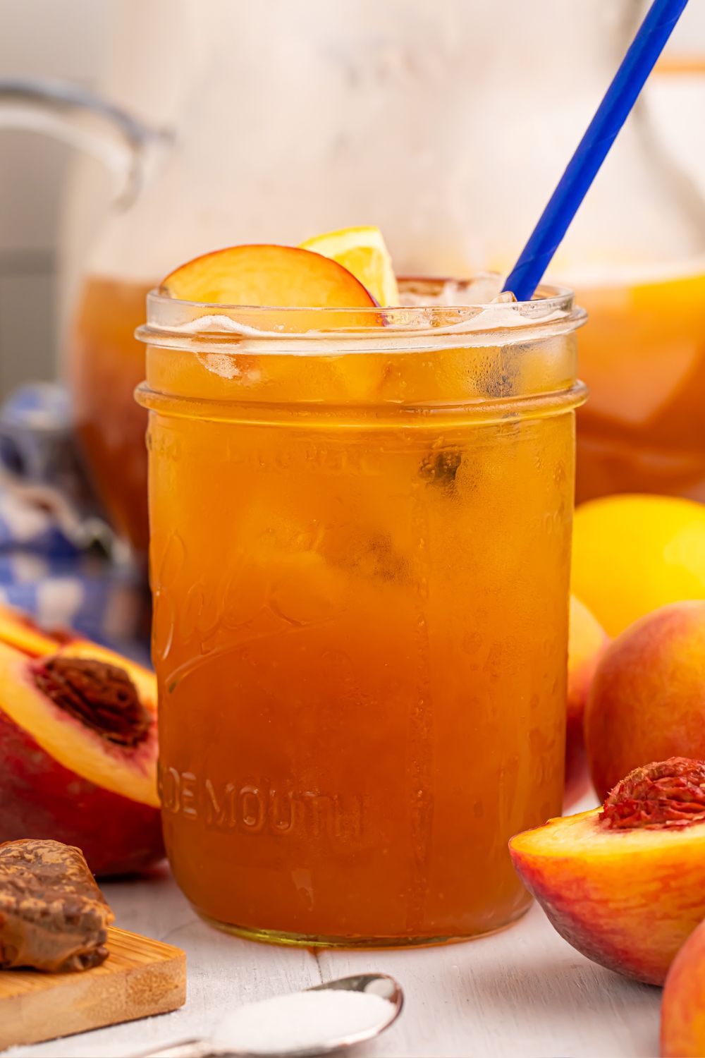 side view of glass full of peach sweet tea with fruit around the glass on table