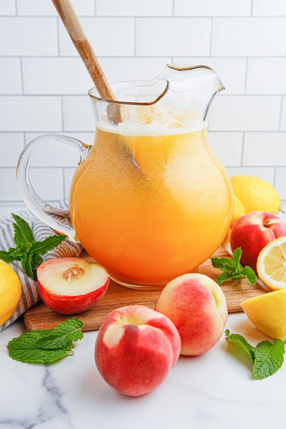 wooden spoon in the pitcher of Peach Lemonade and fresh sliced peaches and lemons around the container