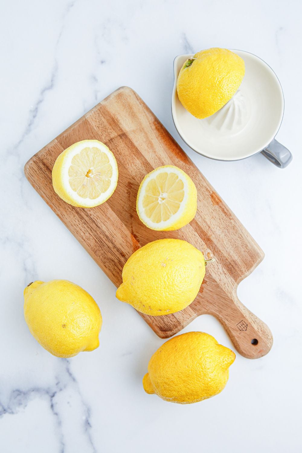 fresh lemons on wooden cutting board. some are cut and a juicer is sitting next to it with half a lemon on it