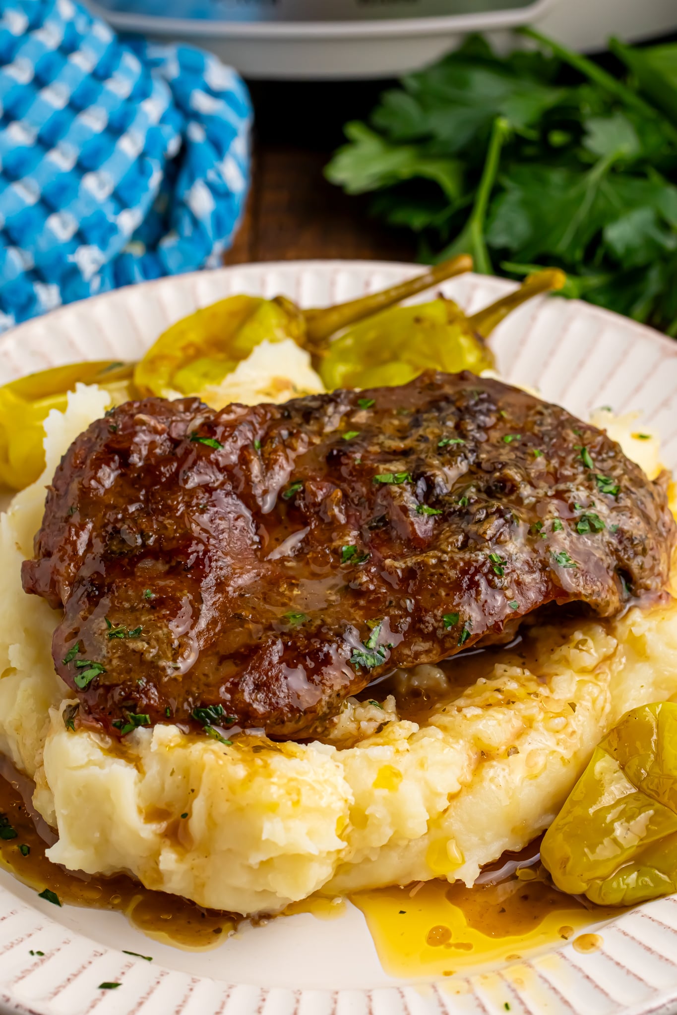 Slow Cooker Mississippi Ribeye Steaks on a white plate, on top of fluffy mashed potatoes