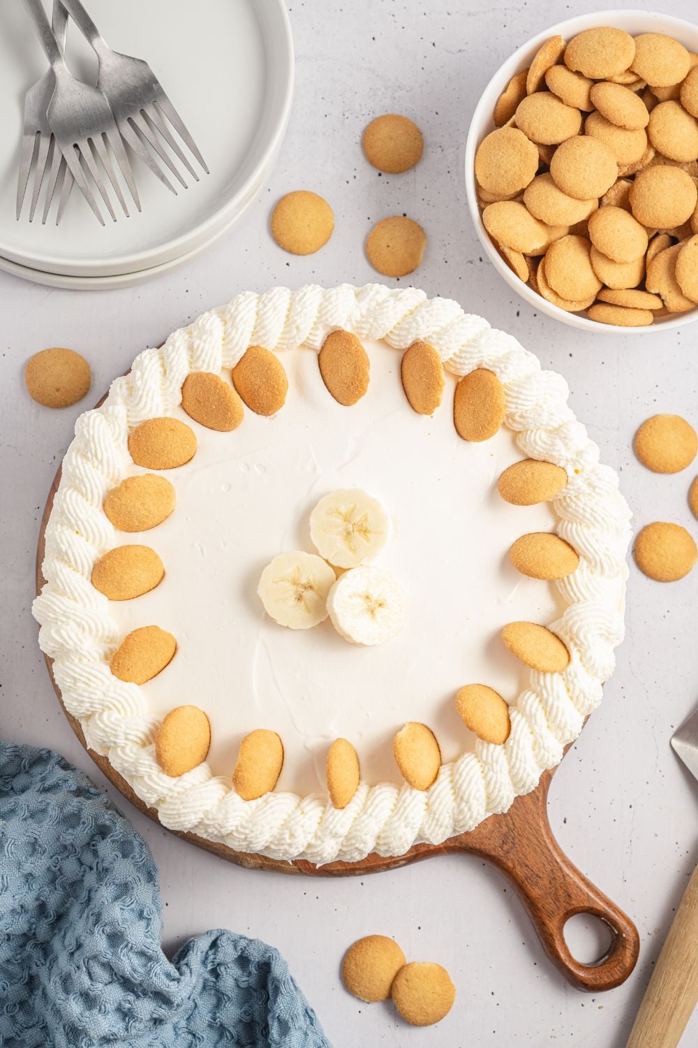 No Bake Banana Pudding Cheesecake on table with wafer cookies around it and a towel