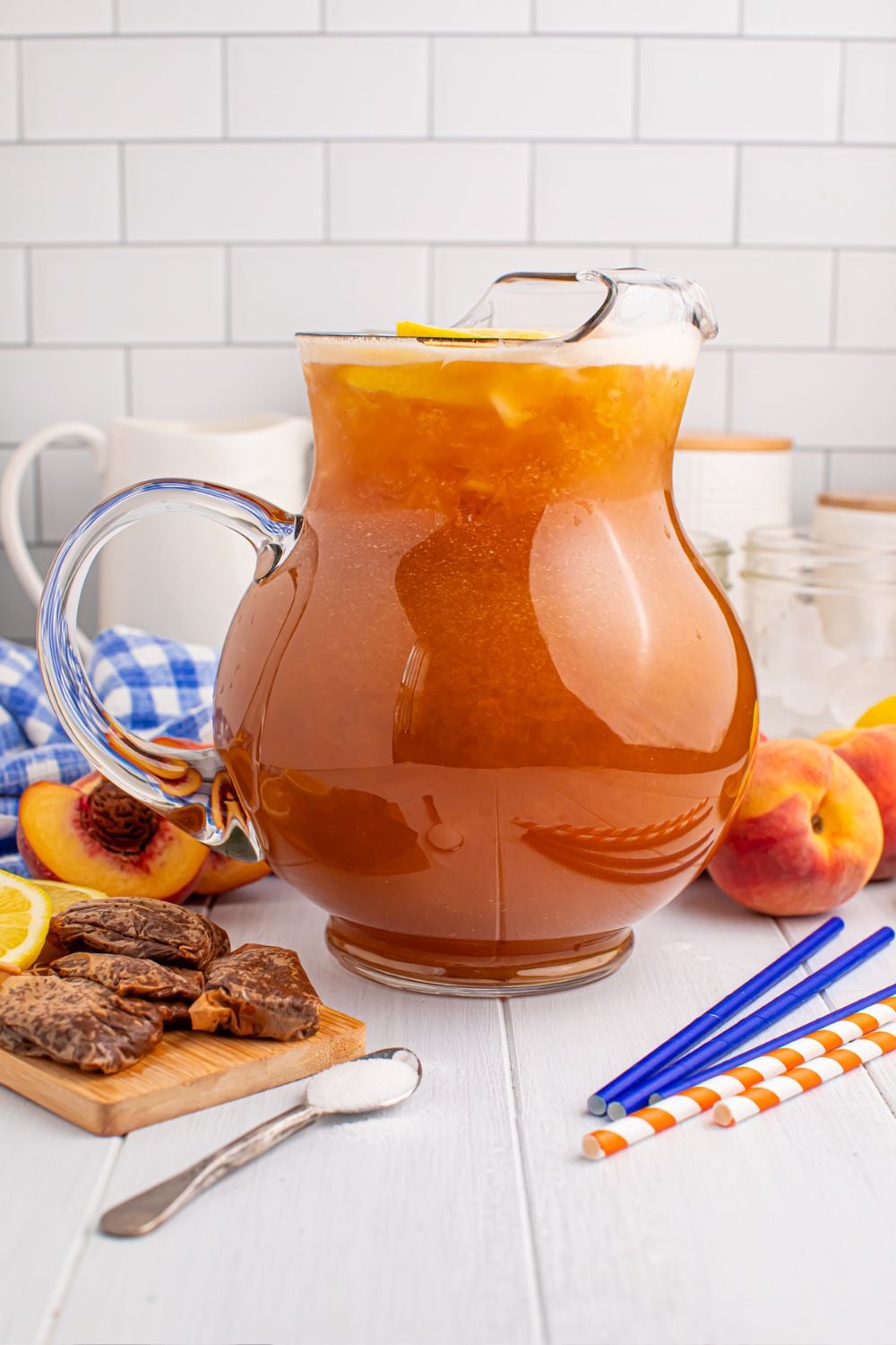 Peach Sweet Tea in a large pitcher with tea bags peaches, and straws around the table