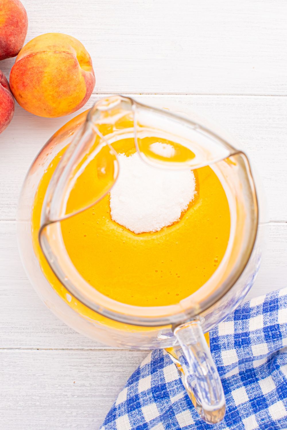 sugar poured into the peach tea mixture in a large pitcher sitting on table