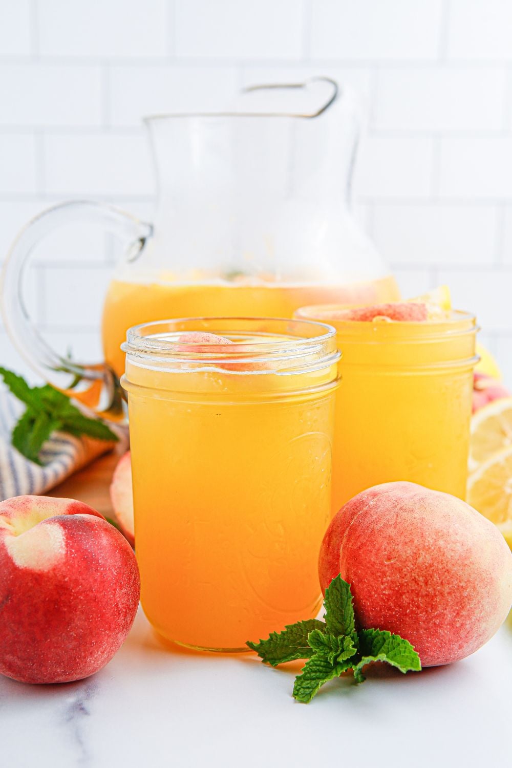 fresh peach lemonade on table in glasses and a glass pitcher as well.