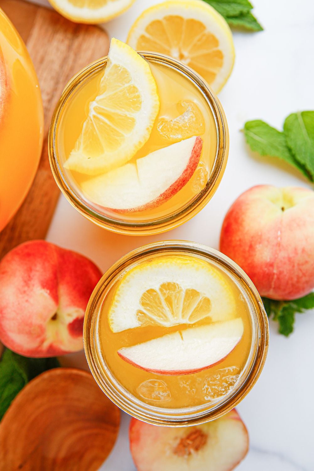 peach lemonade in glasses on table with fresh peaches and sliced lemons on table and mint leaves