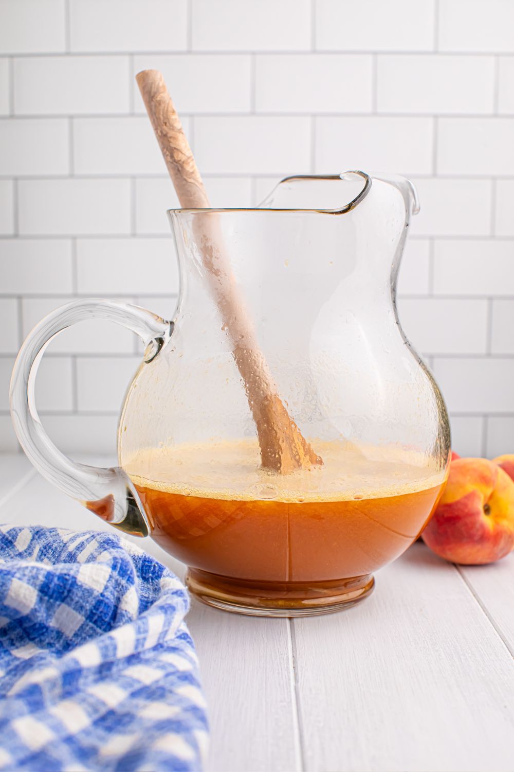 peach blended mixture in a large pitcher being stirred with a wooden spoon