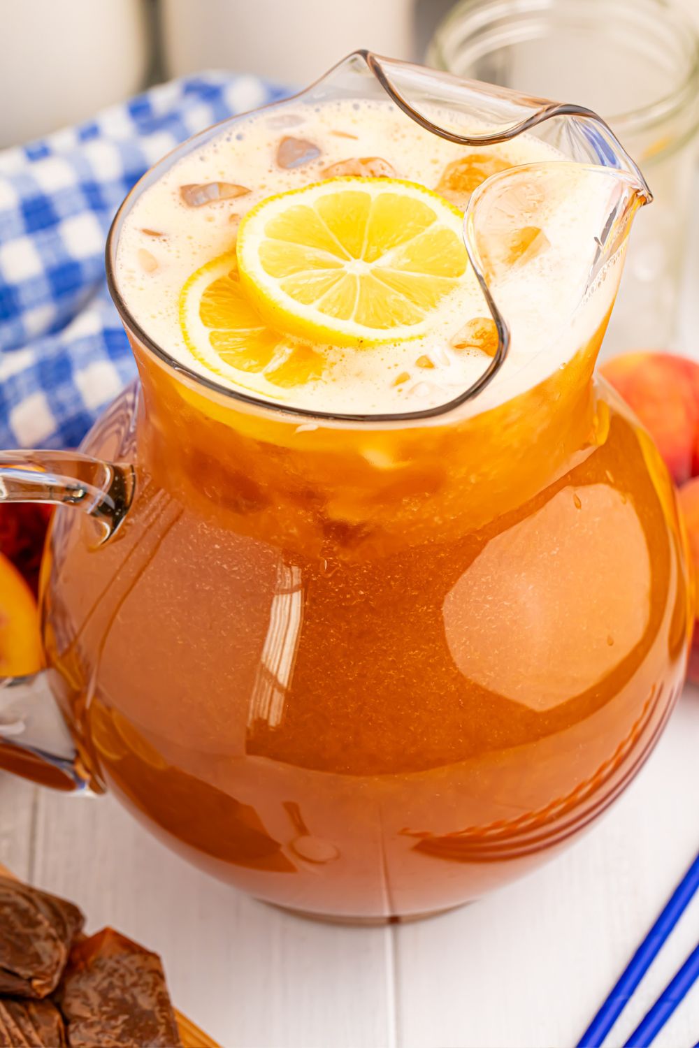 Peach Sweet Tea in a large pitcher on table with a blue napkin and blue straws beside it