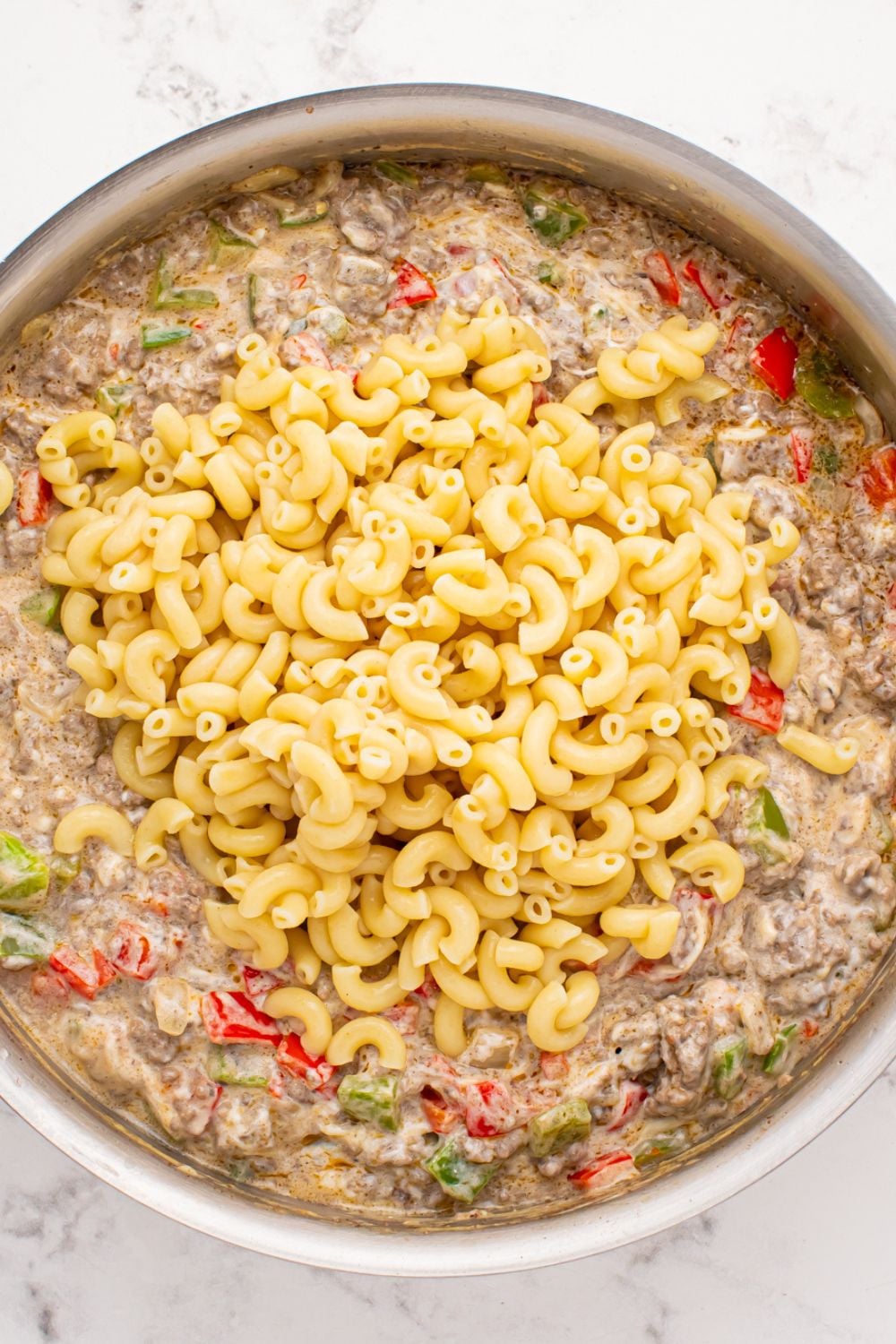 Philly Cheesesteak Pasta mixture in a pan with cooked pasta poured on top of the meat mixture 