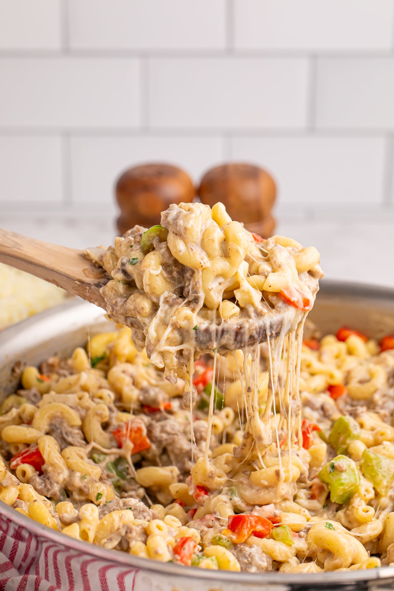 cheese steak pasta in a silver skillet with a wooden spoon lifting up a portion