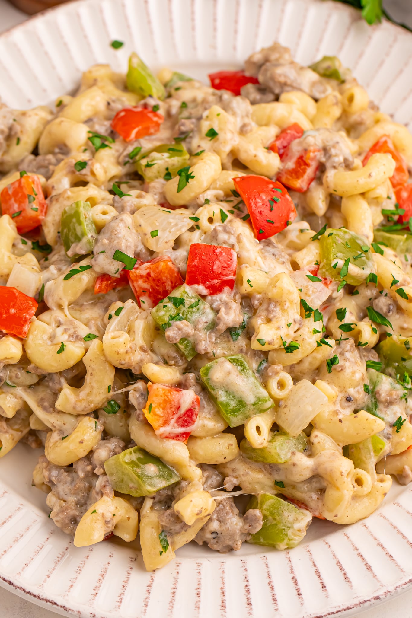 cheese steak pasta on a plate with parsley and cheese around the plate on table