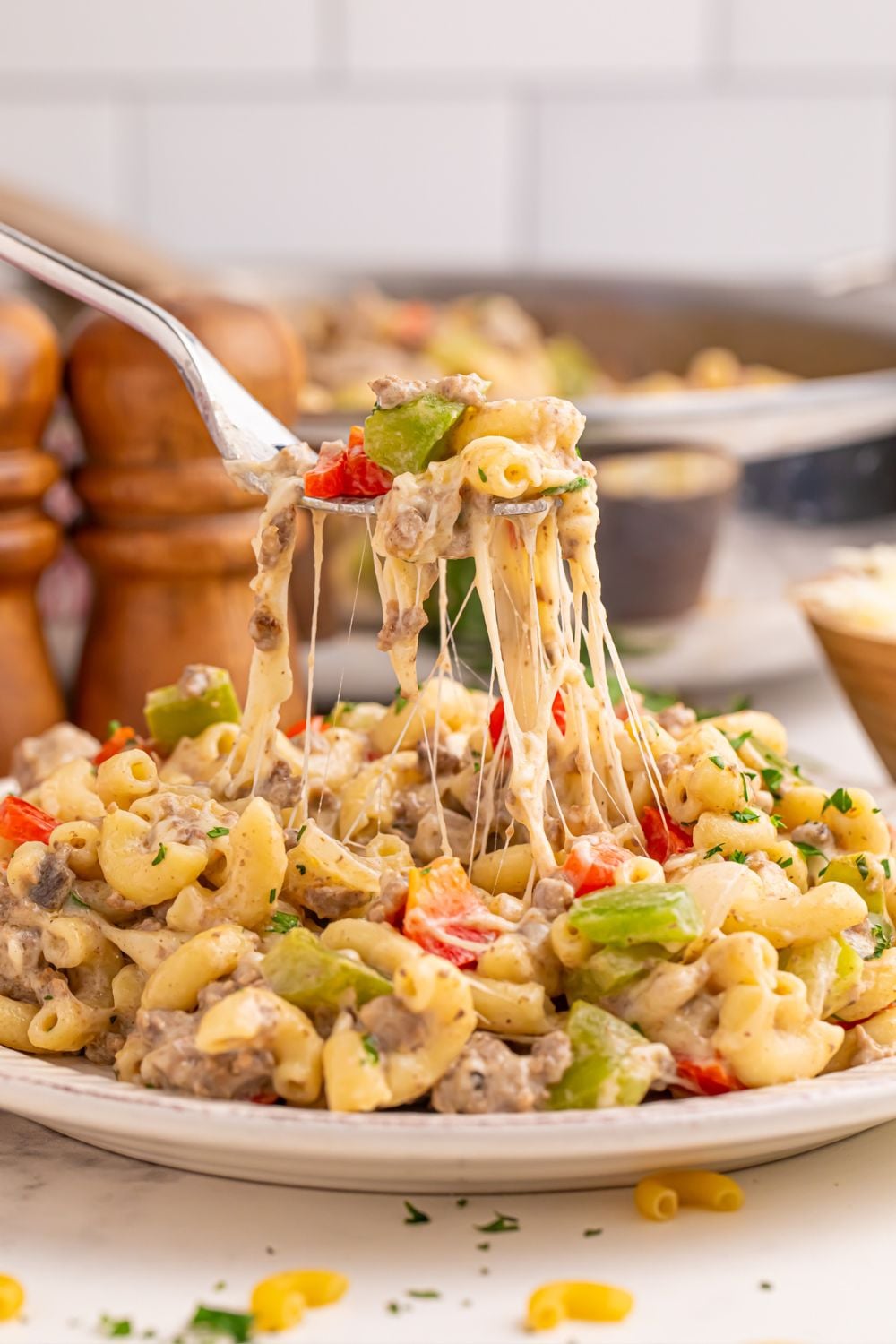 Philly Cheesesteak Pasta on a plate with a fork full pulling up showing the strings of cheese 