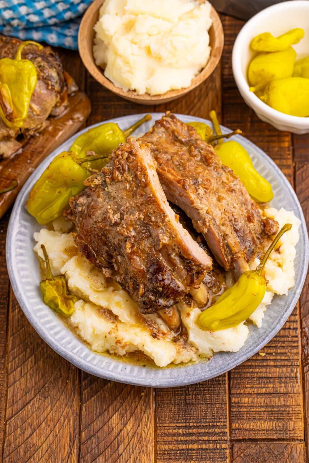 Slow Cooker Mississippi Ribs on a plate with potatoes, and then small bowls with ingredients used to make the pork ribs