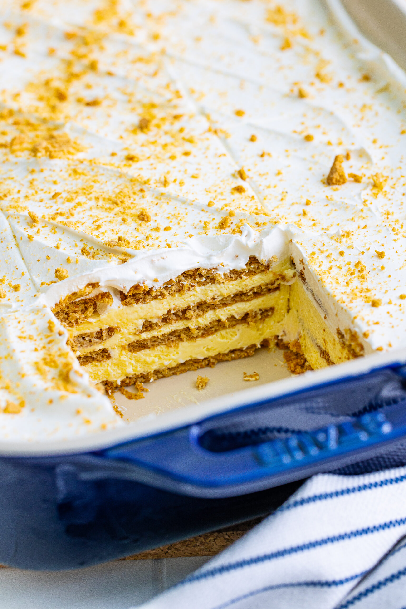 No Bake Banana Icebox Cake in a blue baking dish with a slice removed , topped with crushed vanilla wafers
