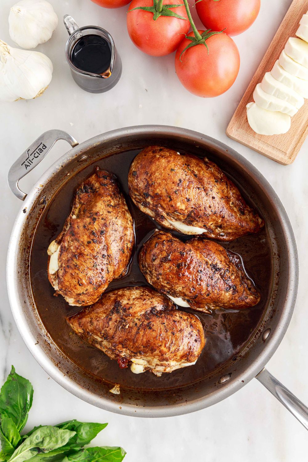 Caprese Stuffed Chicken in a skillet on table with tomatoes, cheese, basil and more around it 