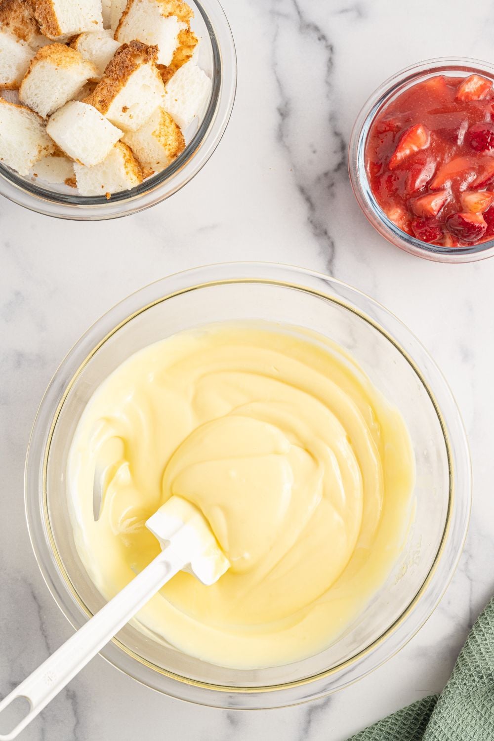 vanilla pudding mixed up in a bowl with strawberries in a bowl and diced angel food cake in another bowl