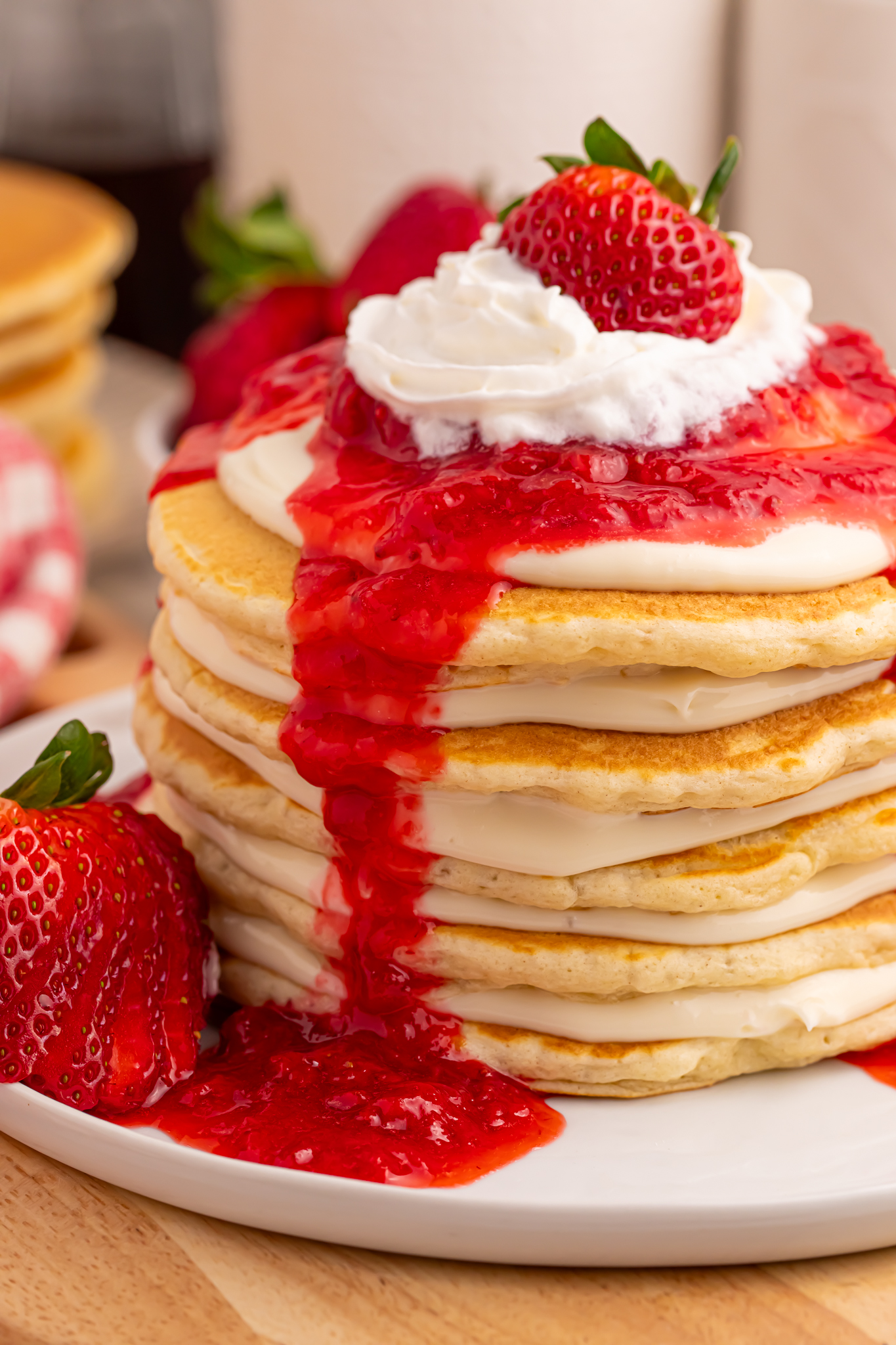 Strawberry Cheesecake Pancakes on a white plate with strawberry sauce drizzled overtop
