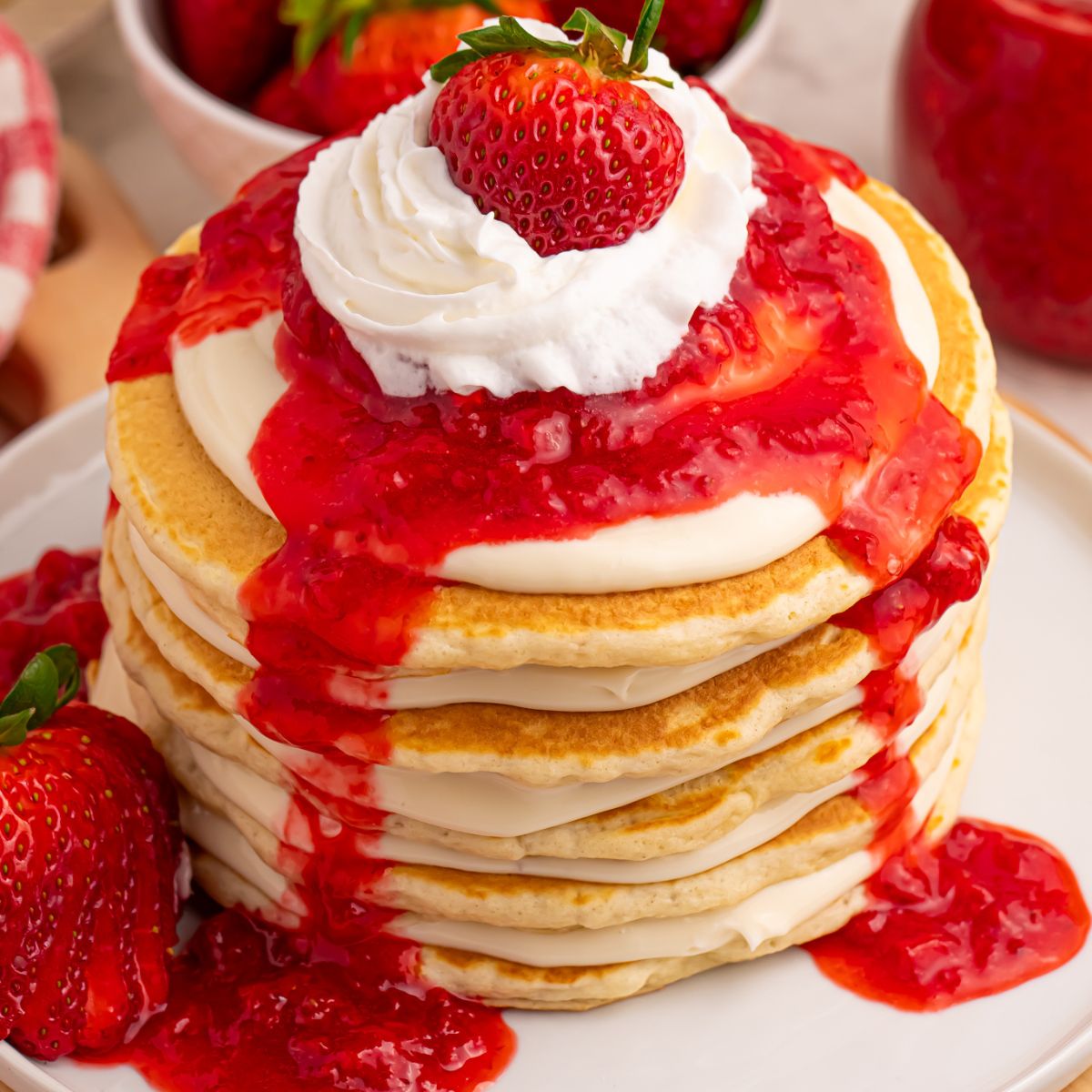 Strawberry Cheesecake Pancakes stacked on a plate with whipped cream a whole berry on top