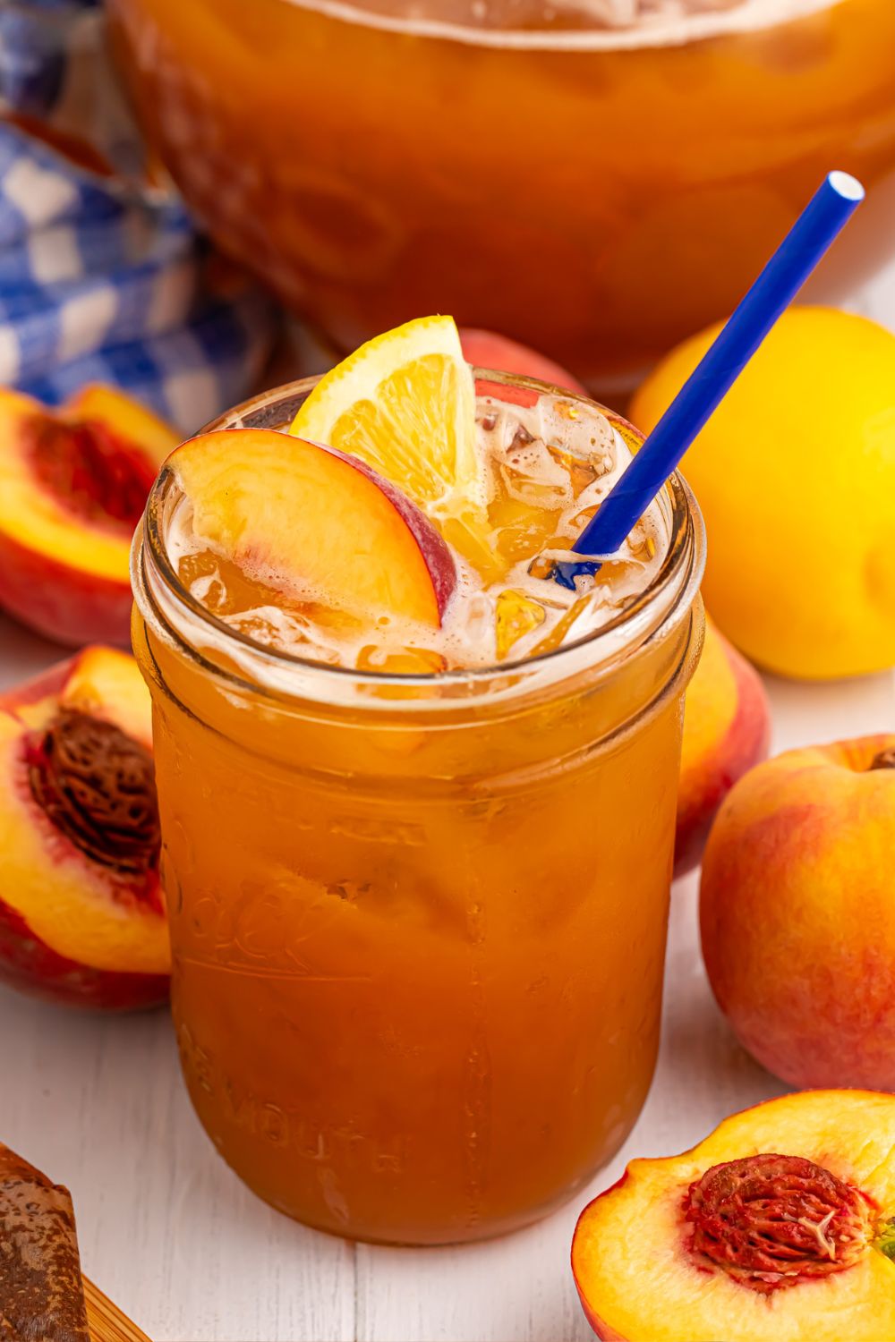 glass of sweet peach tea and sliced peaches all around it on table