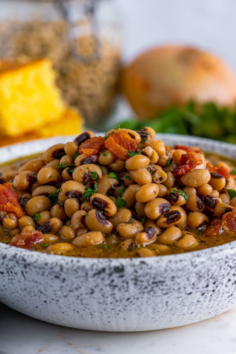 Black Eyed Peas in a bowl on the table with some ingredients and cornbread in the background 